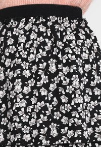 Falda de tela negra con un patrón floral en blanco y rosa claro, que presenta una cintura fruncida y una textura suave.