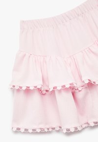 Falda con volantes de suave tela rosa, con una cinturilla elástica y un delicado dobladillo con borde ondulado. Superficie texturizada con volantes en capas.