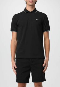 Polo nero con accenti bianchi e azzurri chiari sul colletto e sulle maniche, con un logo. Abbinato a pantaloni corti neri.