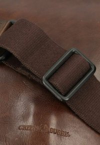Borsa in pelle marrone con una fibbia in metallo nero e una tracolla in tessuto scuro. Il logo impresso "GREEN BURY" è visibile sulla pelle.