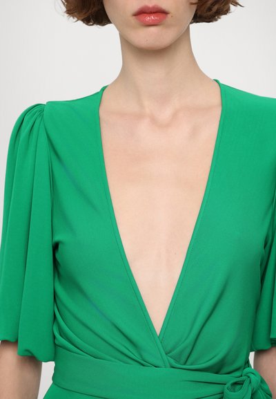 Green dress with a deep V-neck, puffed sleeves, and wrap design. Made of smooth fabric with a tied waist detail.