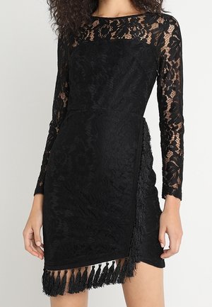 Robe en dentelle noire à manches longues, corsage ajusté, détail en franges à l'ourlet, et motifs floraux sur toute la robe. Texture douce et coupe moulante.