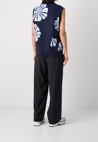 Marineblaues ärmelloses Stricktop mit hellblauen Blumenmustern; kombiniert mit schwarzen Nadelstreifenhosen und weißen Sportschuhen.