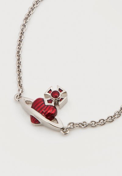Ασημένιο κολιέ με αλυσίδα που φέρει μια κόκκινη καρδιά με κάθετες ρίγες, περιβαλλόμενη από δαχτυλίδι πλανήτη, τονισμένο με ένα μικρό κόκκινο πολύτιμο λίθο.
