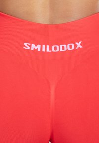 Rode geribde leggings met hoge taille. Bevat een wit "SMILODOX" logo op de tailleband. Soepele textuur, strakke pasvorm.