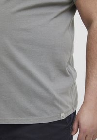 Grijze katoenen T-shirt met korte mouwen, een ronde halslijn en een klein logo label aan de zoom. Soepele textuur en een iets losse pasvorm.