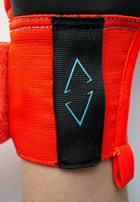 Support de cheville en néoprène de couleur orange vif avec une sangle noire réglable. Présente un logo en forme de diamant bleu sur la surface de la sangle.