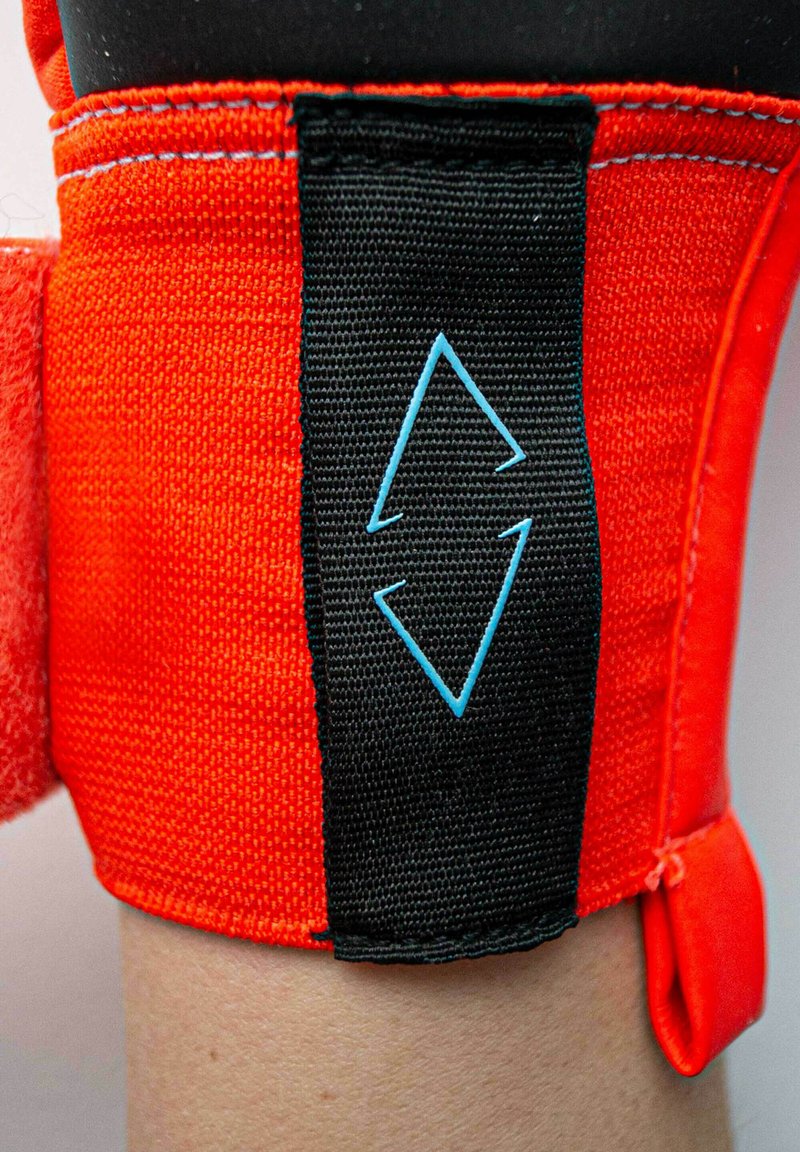 Support de cheville en néoprène de couleur orange vif avec une sangle noire réglable. Présente un logo en forme de diamant bleu sur la surface de la sangle.