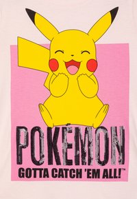 Yellow Pikachu graphic on a light pink t-shirt, with bold black "POKEMON" text and "GOTTA CATCH 'EM ALL!" in a stylish font below.