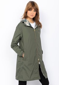 Giacca leggera, impermeabile, verde oliva con cappuccio, decorata con un motivo mimetico, chiusura con zip e due tasche laterali.