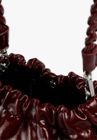Bolso de mano de piel burdeos con textura fruncida, correa de hombro trenzada y herrajes plateados. El interior es oscuro con detalles de cierre visibles.