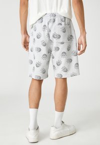 Pantalones cortos grises de tela suave, con un diseño de dibujos animados en negro que se repite. Incluyen un bolsillo trasero y una cinturilla elástica para mayor comodidad.