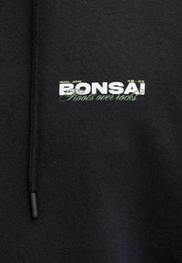 Schwarzer Stoff mit schwarzem Kordelzug, versehen mit weißem und grünem Text "Osaka Japan BONSAI Roots over rocks" sowie japanischen Schriftzeichen.