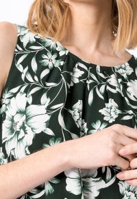 Débardeur floral avec un imprimé vert et blanc, corsage plissé et encolure ronde. Le tissu semble léger avec une texture lisse.