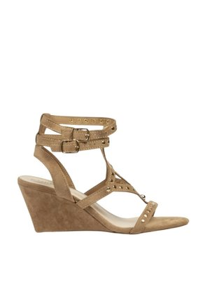 Sandalia de cuña de ante beige con doble pulsera en el tobillo y hebillas, tira en los dedos y perforaciones decorativas sobre fondo blanco.