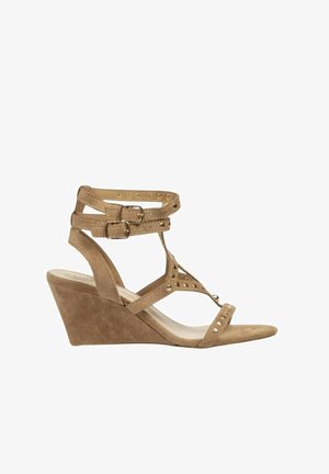 Sandalia de cuña de ante beige con doble pulsera en el tobillo y hebillas, tira en los dedos y perforaciones decorativas sobre fondo blanco.