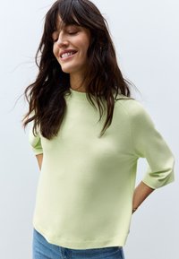 Light green, soft-textured sweater with a crew neck and three-quarter sleeves, paired with blue denim jeans. Simple and casual design.