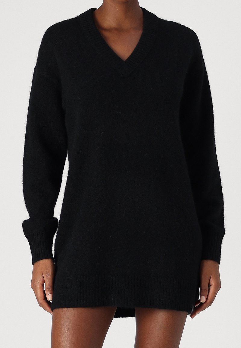 Robe-pull noire à col en V, confectionnée en tissu tricoté doux, avec manches longues et détails côtelés aux poignets et à l'ourlet. Design simple et classique.