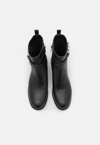 Une paire de bottines noires en cuir avec des zips latéraux et des sangles décoratives, vues de dessus sur un fond blanc.