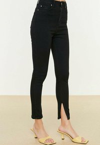 Czarne dżinsy z wysokim stanem o dopasowanym kroju, z zamkiem błyskawicznym z przodu, bocznymi rozcięciami u dołu oraz subtelnymi detalami w szwie.