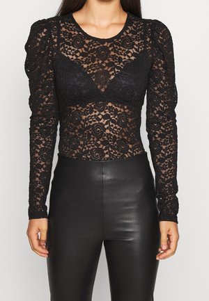 Schwarzes langärmliges Spitzen-Top mit Blumenmuster und aufgepufften Schultern, getragen zu hoch taillierter schwarzer Lederhose, gezeigt von Hals bis Hüfte.