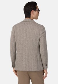 Beige kavaj i fiskbensmönster med skräddarsydd passform, strukturerade axlar och två knappar på ärmarna; slät textur.