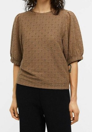 Blouse marron texturé avec un motif de vagues subtil, manches courtes bouffantes, col rond, portée avec un pantalon noir.