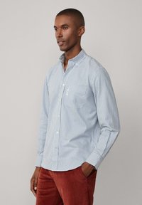 Camisa de botones a rayas azul y blanca con cuello y un único bolsillo en el pecho, hecha de un tejido ligero, exhibida en un modelo.