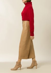 Rode coltrui, geribbelde manchetten, gecombineerd met beige leren wijde broek en nude enkellaarsjes met vierkante neuzen en ritssluitingen aan de zijkant.