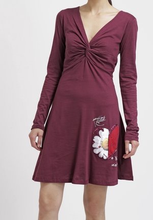 Robe bordeaux à manches longues avec un décolleté en V profond torsadé et un motif de marguerite au cœur rouge sur la partie inférieure de la jupe.