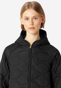 Chaqueta negra acolchada con capucha, con una textura suave, patrón de costura en ondas y un zipper dorado en la parte delantera.