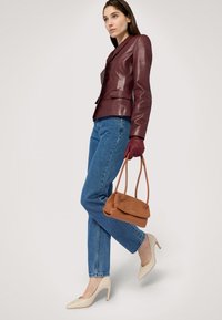 Burgundské kožené sako, modré džíny, béžové vysoké podpatky, hnědá kabelka. Modelka stojí s jednou nohou vpřed a má na sobě rukavice.