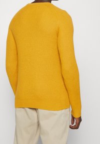 Gelber gerippter Strickpullover mit langen Ärmeln und rundem Ausschnitt, mit strukturierter Oberfläche und geradem Saum.