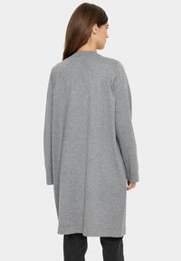 Cardigan lungo grigio chiaro con una vestibilità rilassata, texture morbida, apertura frontale e maniche lunghe, caratterizzato da un design semplice e lineare.