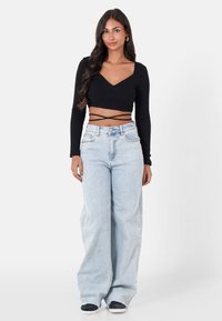 Czarny prążkowany crop top z długim rękawem, z kwadratowym dekoltem i oplatającymi paskami, w zestawieniu z jasnoniebieskimi spodniami dzwonami i czarnymi sneakersami.
