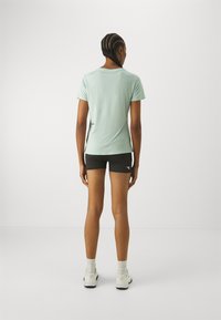 T-shirt atletica verde chiaro con maniche corte, abbinata a pantaloni corti neri. Il tessuto appare liscio e leggero, ideale per l'abbigliamento sportivo.