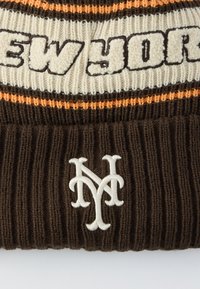 Barna kötött sapka krémszínű és narancssárga csíkokkal. Vastag betűkkel "NEW YORK" felirattal és fehér hímzett NY logóval. Bordázott textúrával.