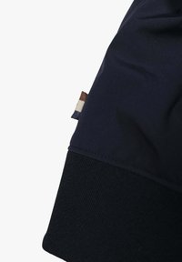 Felpa di un blu navy scuro con una texture liscia, polsini a coste e un piccolo etichetta di marca in beige, marrone e blu presso la cucitura.