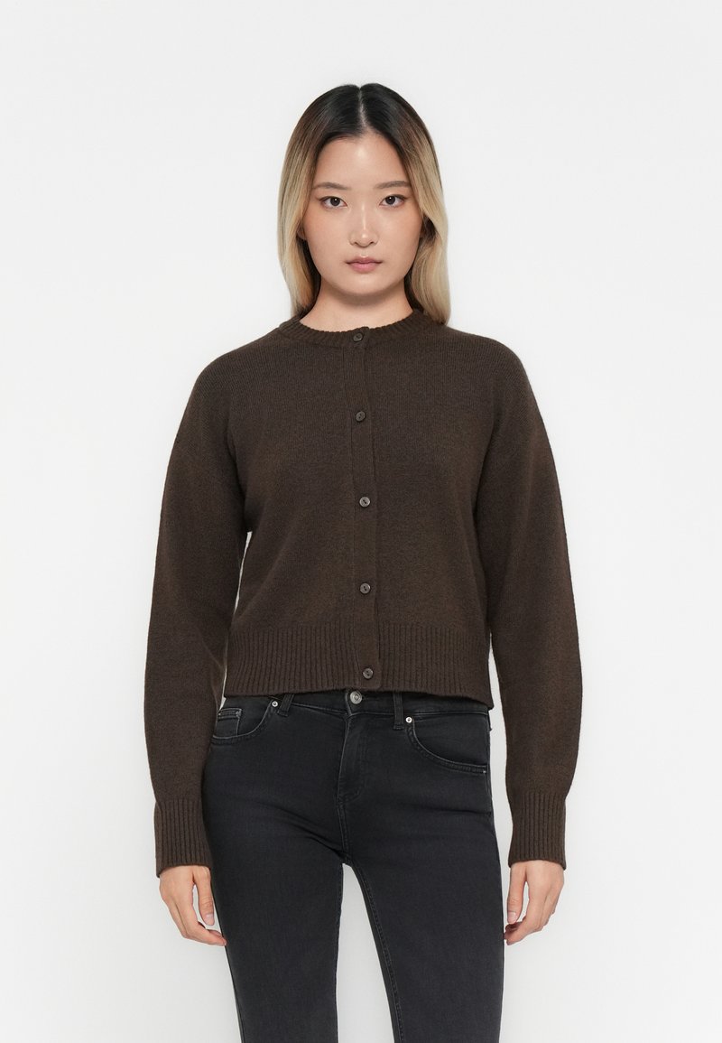 Bruine gebreide cardigan met een ronde hals, geribde manchetten en zoom, voorzien van een knoopsluiting aan de voorkant. Draag het over zwarte jeans.