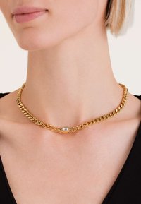 Gouden ketting met een dik, in elkaar vergrendeld ontwerp en een centrale rechthoekige kristalaccent. Glad oppervlak, glanzende afwerking.