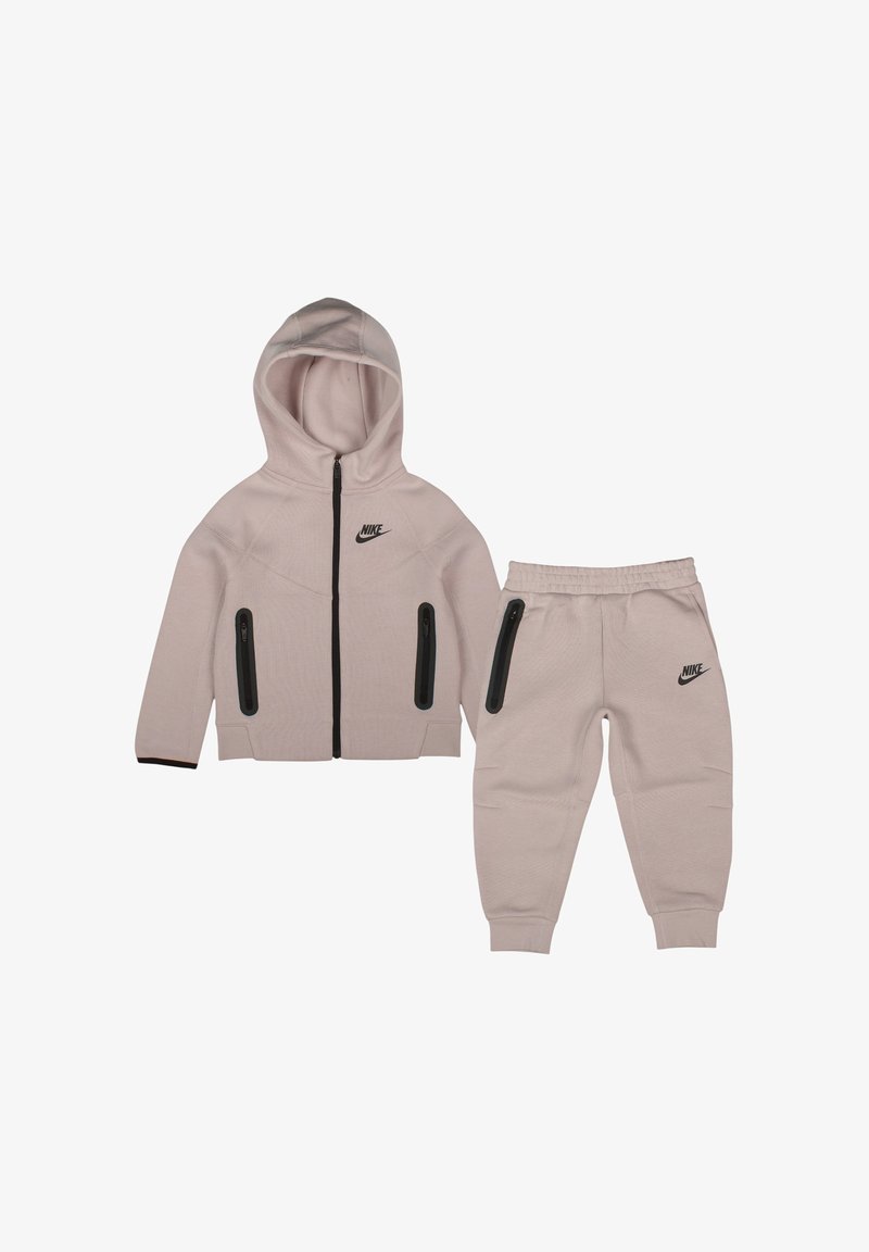 Survêtement pour enfant Nike beige clair composé d'une veste à capuche avec poches zippées noires et d'un pantalon de jogging assorti avec taille et poignets élastiques.