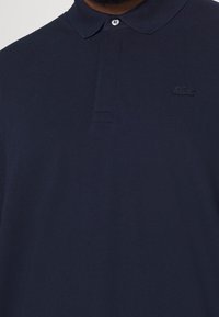 Polo shirt bleu marine en tissu texturé, avec un col, trois boutons et un logo brodé sur la poitrine gauche.