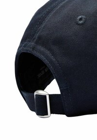 Marinblå keps med en texturerad tyg, böjd skärm och justerbart metalldrag i ryggen. Sömmarna är synliga längs kanterna.