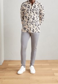 Lightweight button-up shirt with a cream base and black leaf pattern, paired with slim grey pants and white sneakers.