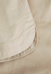 Tela beige con una textura suave, que presenta un dobladillo doblado y un detalle de costura en contraste. Enfócate en la forma limpia de las capas de tela.