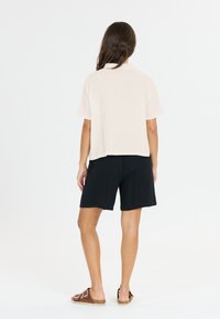 Lichtbeige top met korte mouwen en een relaxte pasvorm, gecombineerd met zwarte shorts met een gestructureerde afwerking. Het schoeisel heeft een platte zool en gespsluiting.