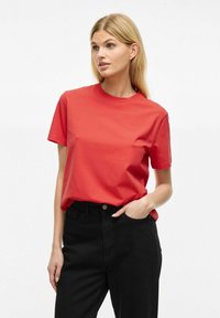 Rød bomulds t-shirt med rund halsudskæring og korte ærmer, parret med sorte højtaljede jeans. Glat tekstur, klassisk pasform.