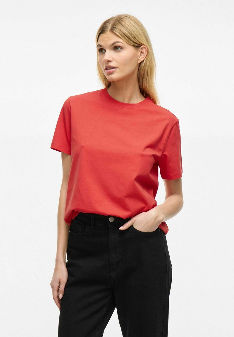 Rød bomulds t-shirt med rund halsudskæring og korte ærmer, parret med sorte højtaljede jeans. Glat tekstur, klassisk pasform.