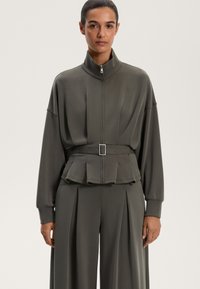 Prevelik temno sivi zip-up jopič z visokim ovratnikom in peplum pasom. Ima dolge rokave in je izdelan iz gladkega, lahkega povoja.