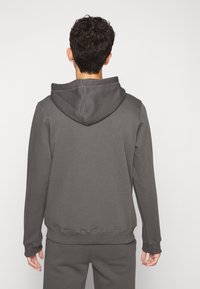 Sweat à capuche gris foncé avec une capuche à cordon, des poignets et un ourlet côtelés. Texture du tissu douce observée de dos, avec des coutures discrètes.